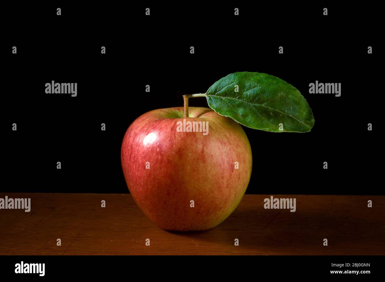 Mela con foglia su superficie di legno su sfondo nero - Foto Stock