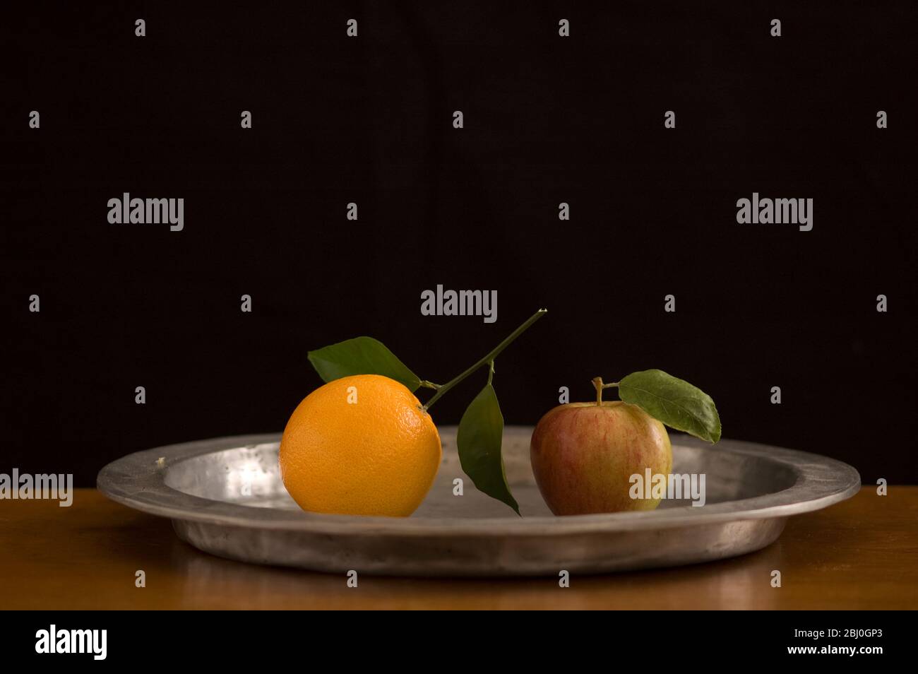 Mela e arancione con foglie su peltro caricabatterie con sfondo nero - Foto Stock