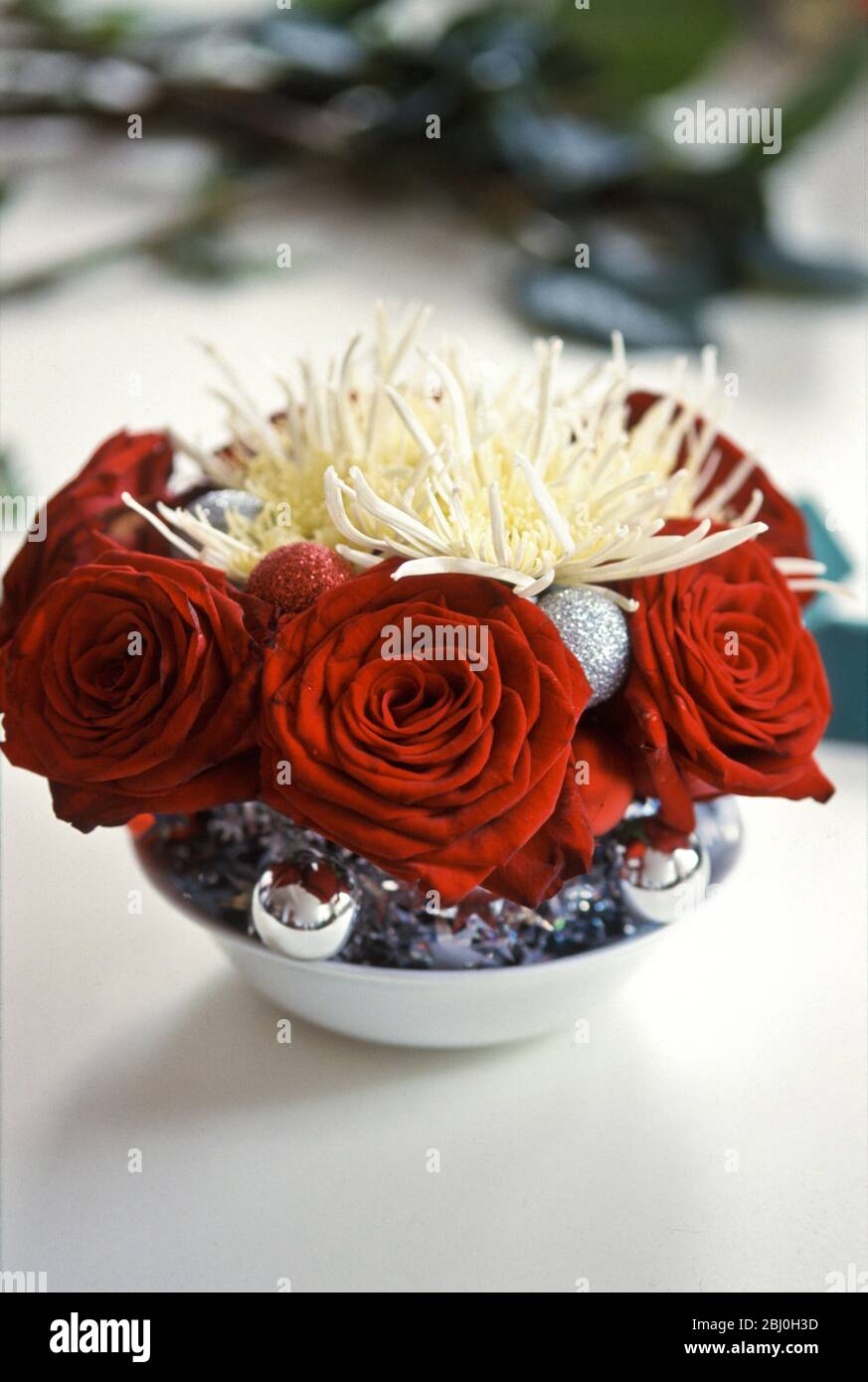 Decorazione di tavola di Natale di rose rosse profonde e crisantemi spiky con baubles d'argento - Foto Stock
