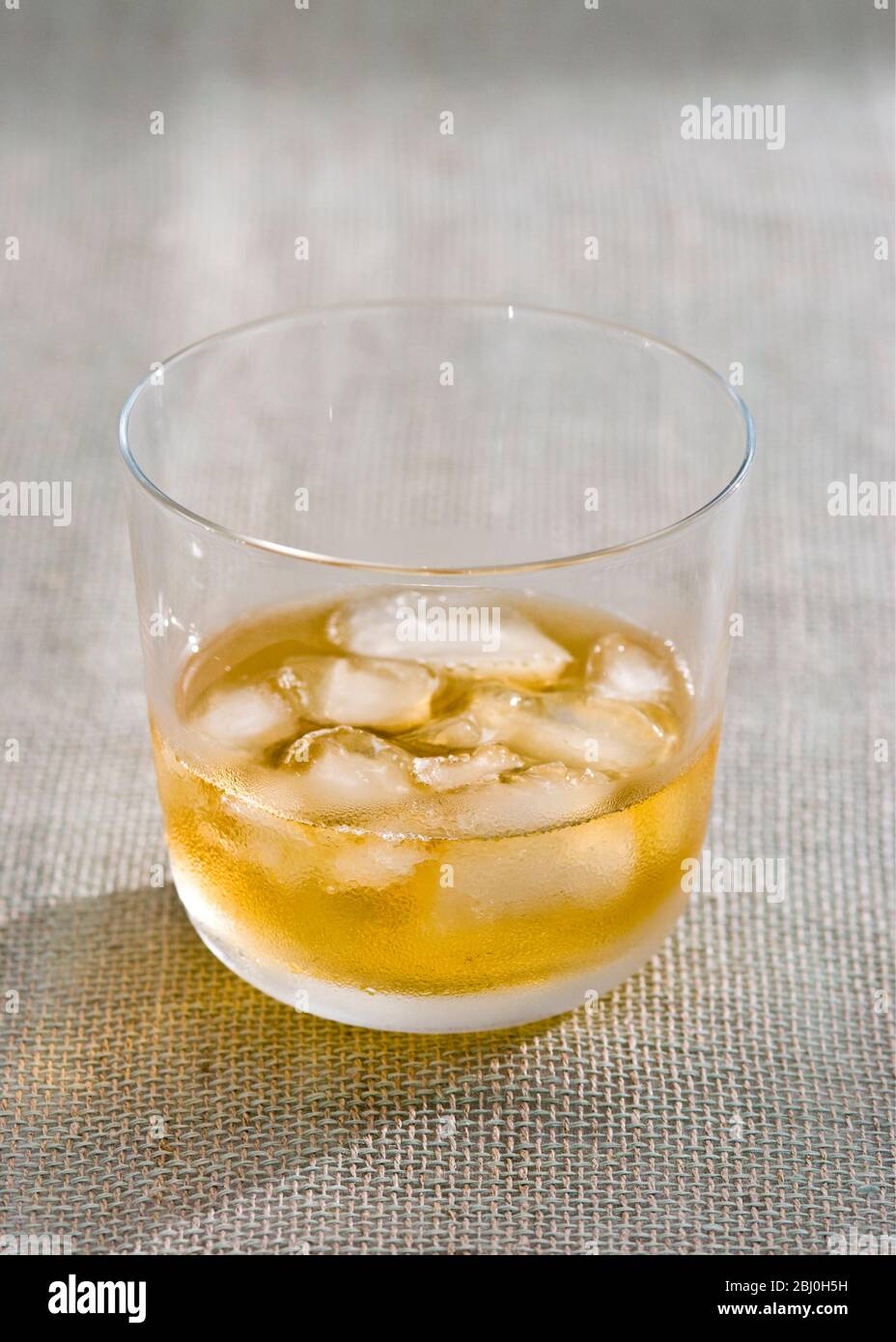 Bicchiere di whisky con ghiaccio su tela hessian ruvida - Foto Stock