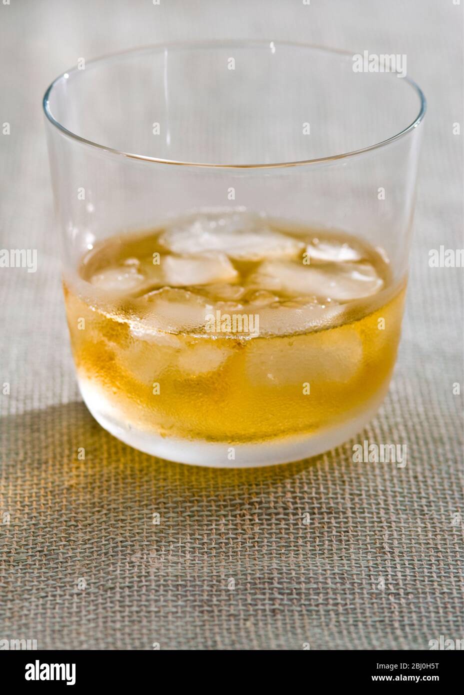 Bicchiere di whisky con ghiaccio su tela hessian ruvida - Foto Stock