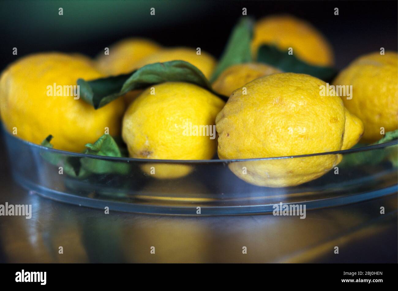 Limoni naturali mediterranei con foglie in vetro su banco in acciaio inox - Foto Stock