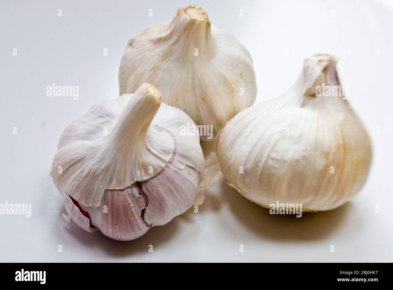 Tre bulbi interi di aglio su superficie bianca - Foto Stock
