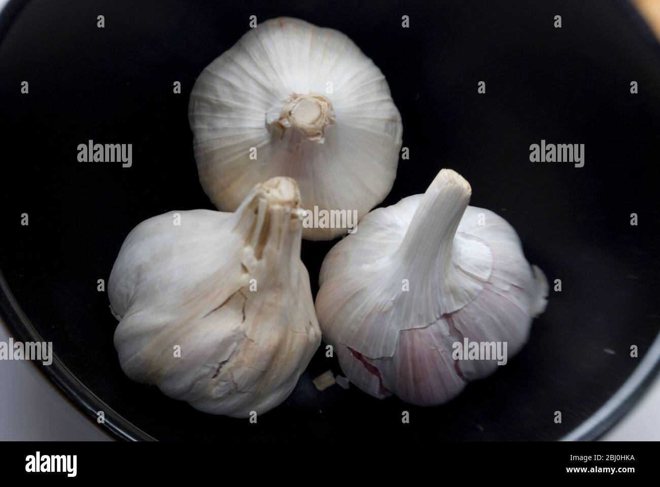 Tre bulbi interi di aglio in ciotola nera - Foto Stock