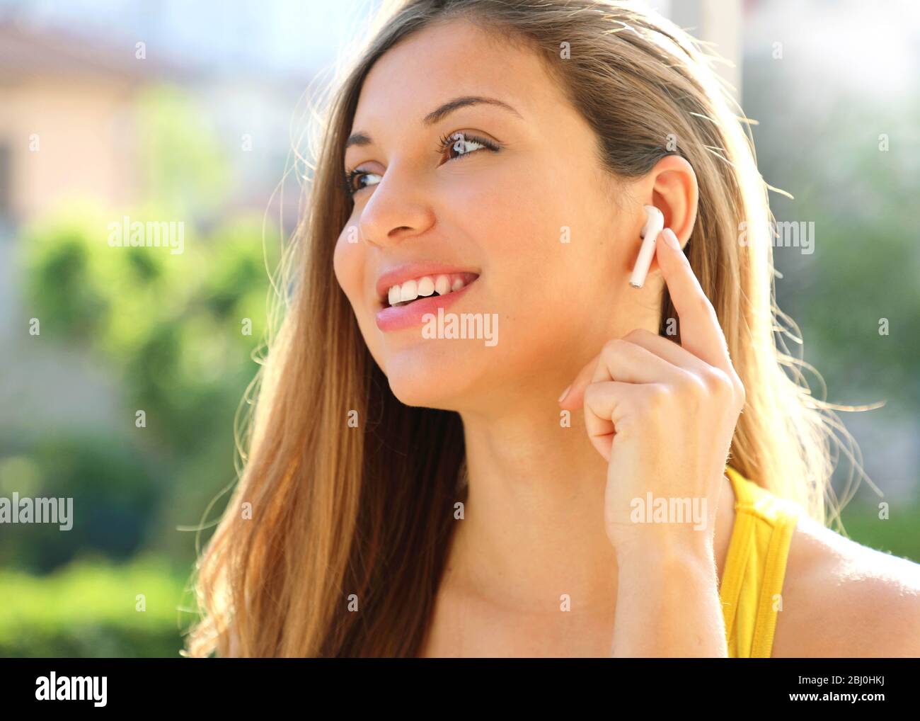 Primo piano di una ragazza sorridente sportiva che collega gli auricolari wireless all'esterno Foto Stock