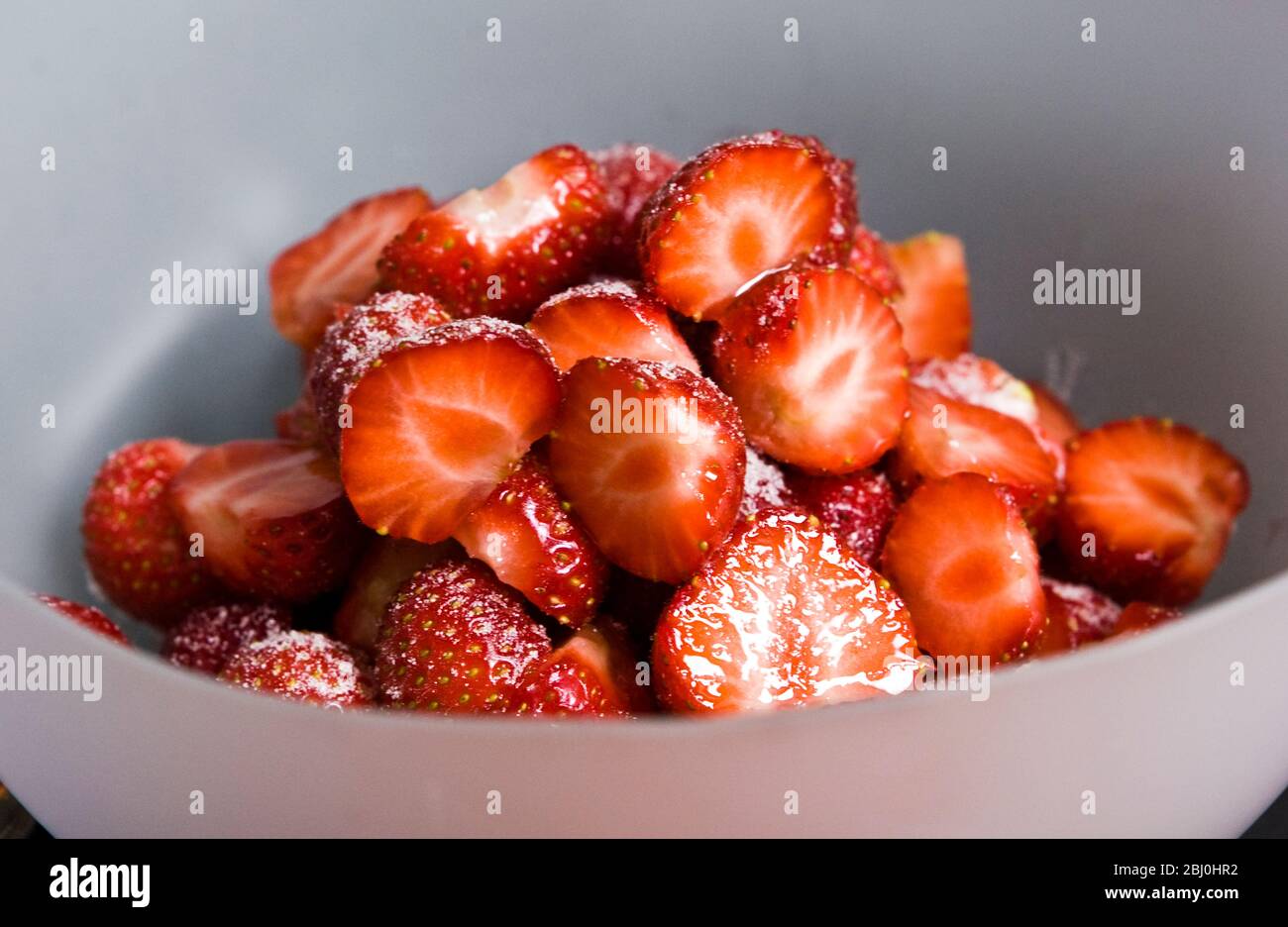 Fragole, spolverate e dimezzate in ciotola, spolverate con zucchero a velo. - Foto Stock