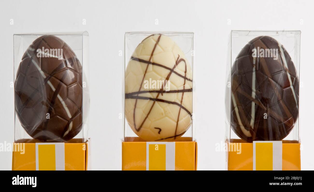 Tre uova di Pasqua simili al cioccolato - cioccolato semplice, al whie e al latte, scatole di cellophane. - Foto Stock