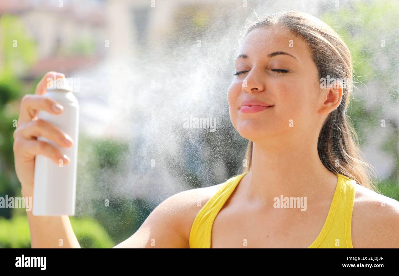Giovane donna che spruzza acqua termale sul suo viso fuori. Acqua termale utilizzata per la cura della pelle, per il trucco, per aiutare irritazione della pelle, arrossamento e punture di insetti. Foto Stock