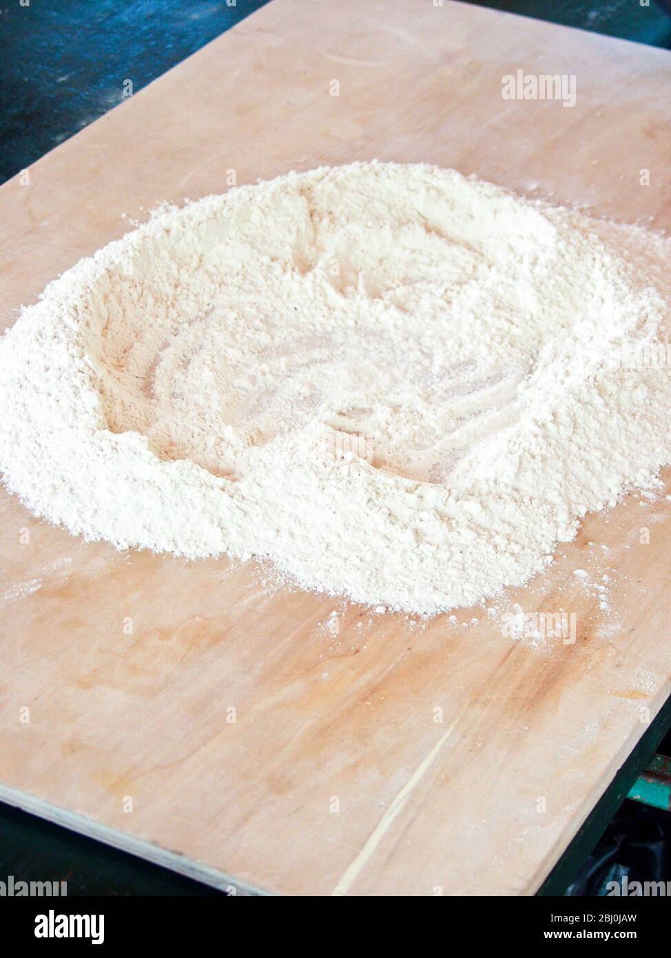 Fare un pozzo di farina su un asse di legno come prima fase di fare gnocchi - Foto Stock