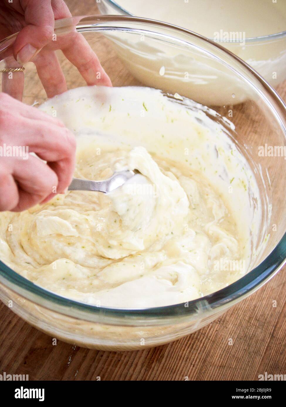 Mescolando la panna montata in crema di uova raffreddata e addensata con gelatina e scorza di lime per il dessert trifle. - Foto Stock