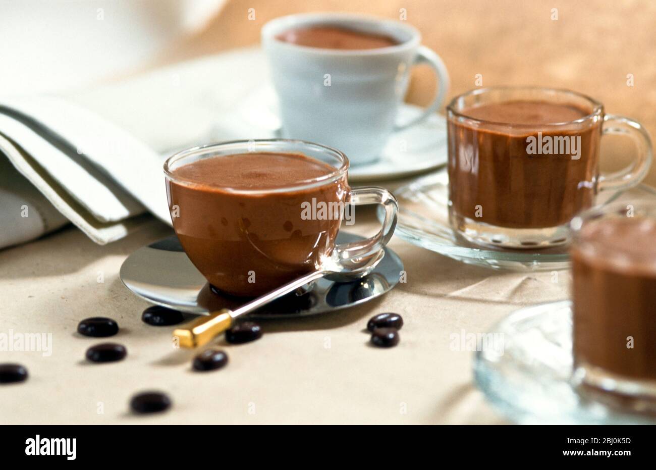 Mousse al cioccolato servita in una varietà di graziose tazze con cioccolatini di chicchi di caffè sparsi intorno al tavolo - Foto Stock