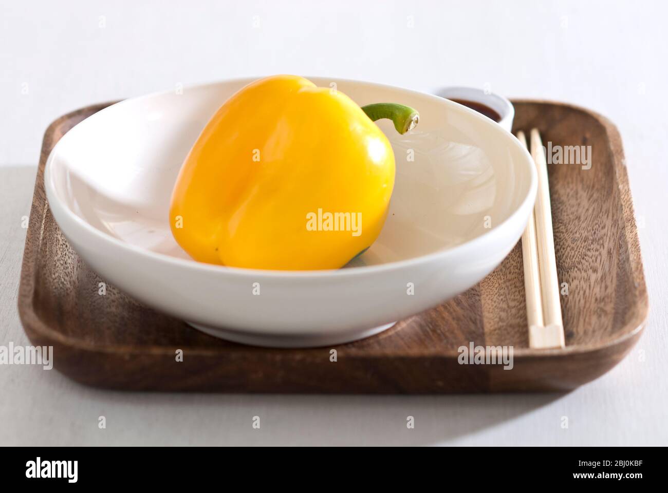 Ciotola bianca su piatto di legno con pepe giallo dolce. - Foto Stock