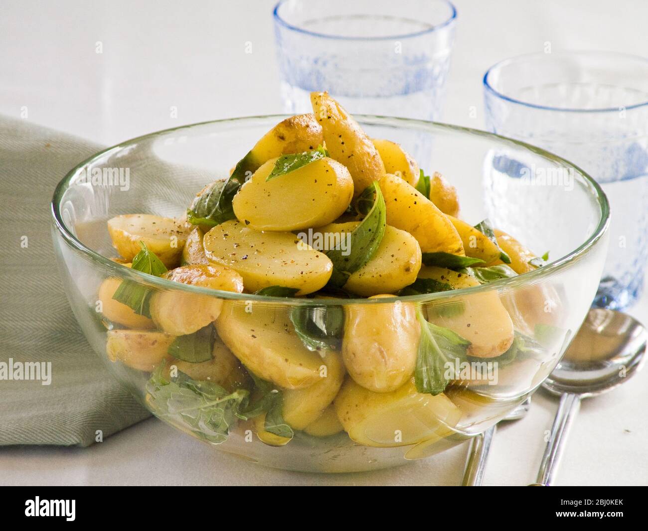 Insalata di patate in condimento con olio d'oliva, aceto di vino e senape integrale, con foglie di basilico - Foto Stock