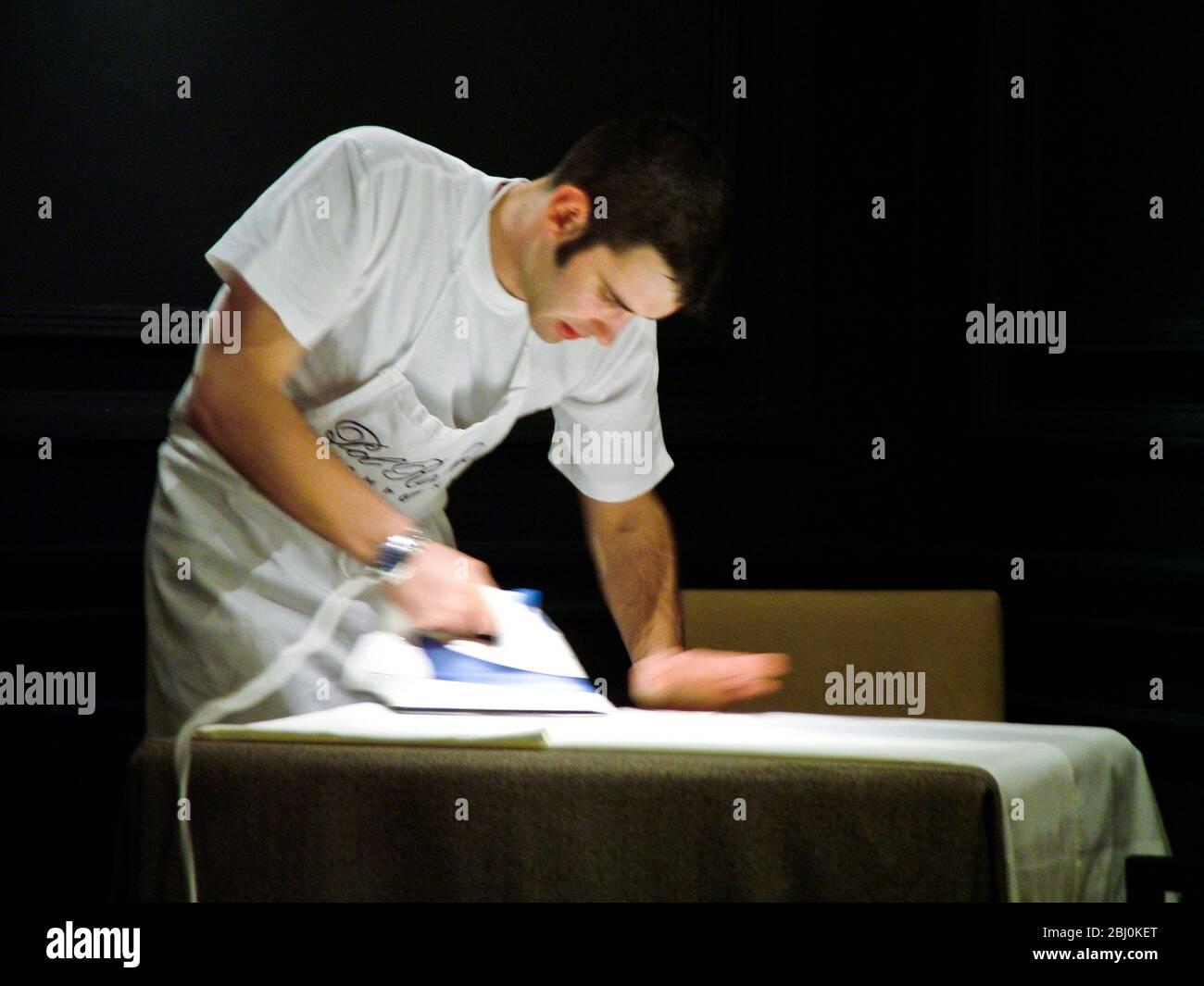 Stiratura di biancheria bianca in biancheria da tavola in interni del ristorante scuro prima del servizio - Foto Stock