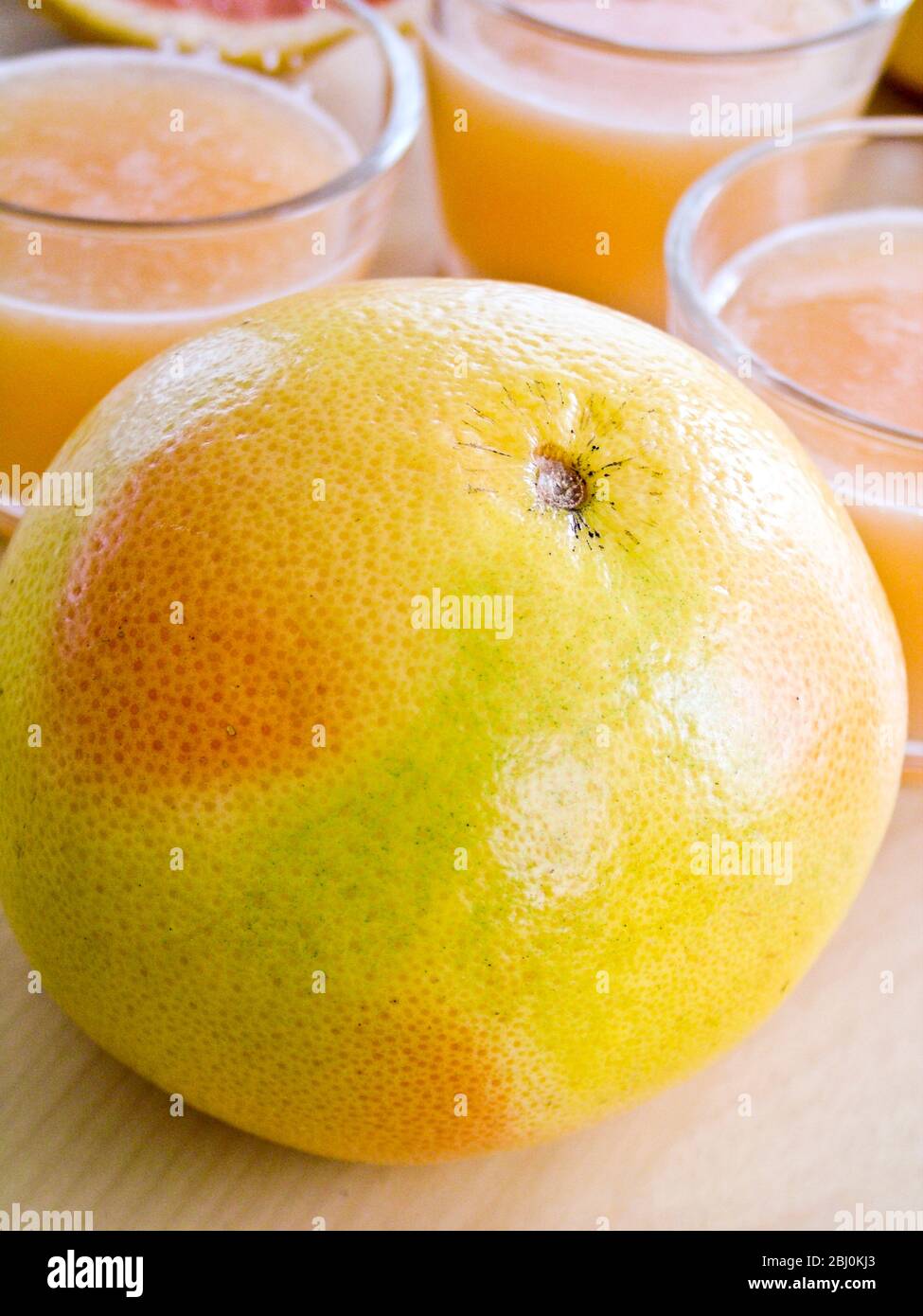 Piccoli bicchieri di succo di pompelmo rosa con pompelmo intero e dimezzato - Foto Stock