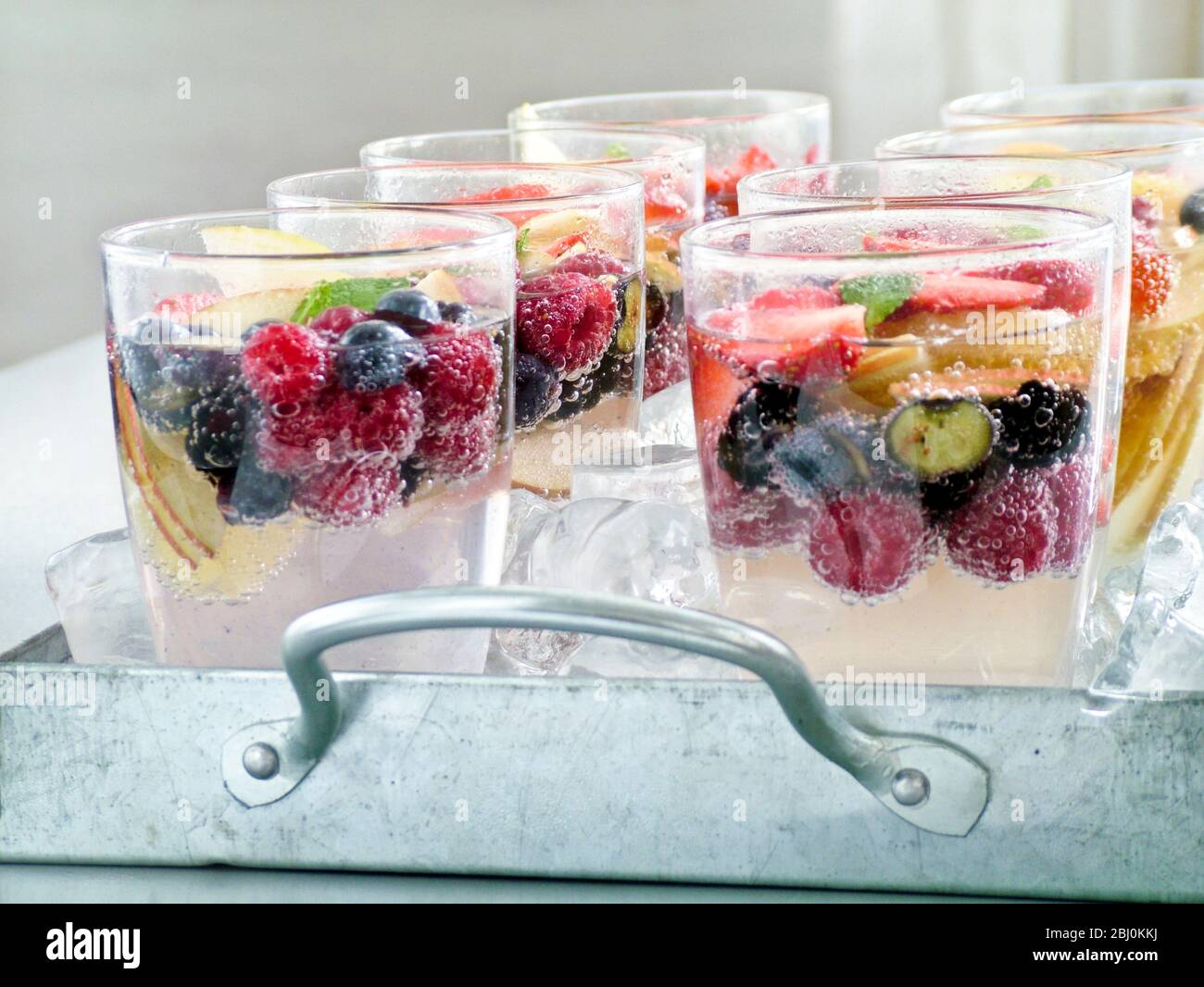 Acqua frizzante con frutta fresca e bacche in bicchieri gon sittin ghiaccio tritato su vassoio di metallo - Foto Stock