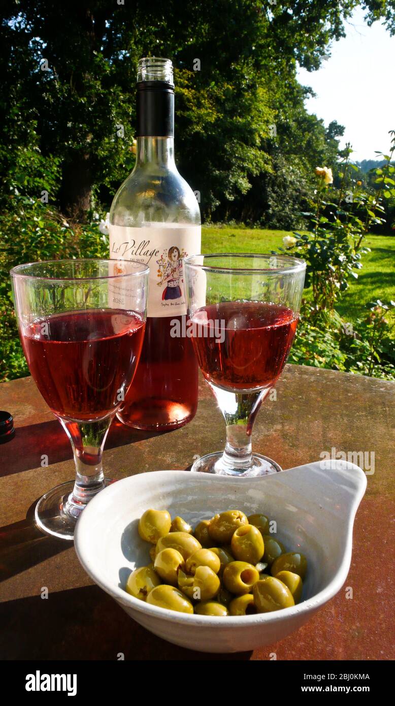 Vino rosato e olive farcite su tavola di ferro arrugginita in giardino di campagna - Foto Stock