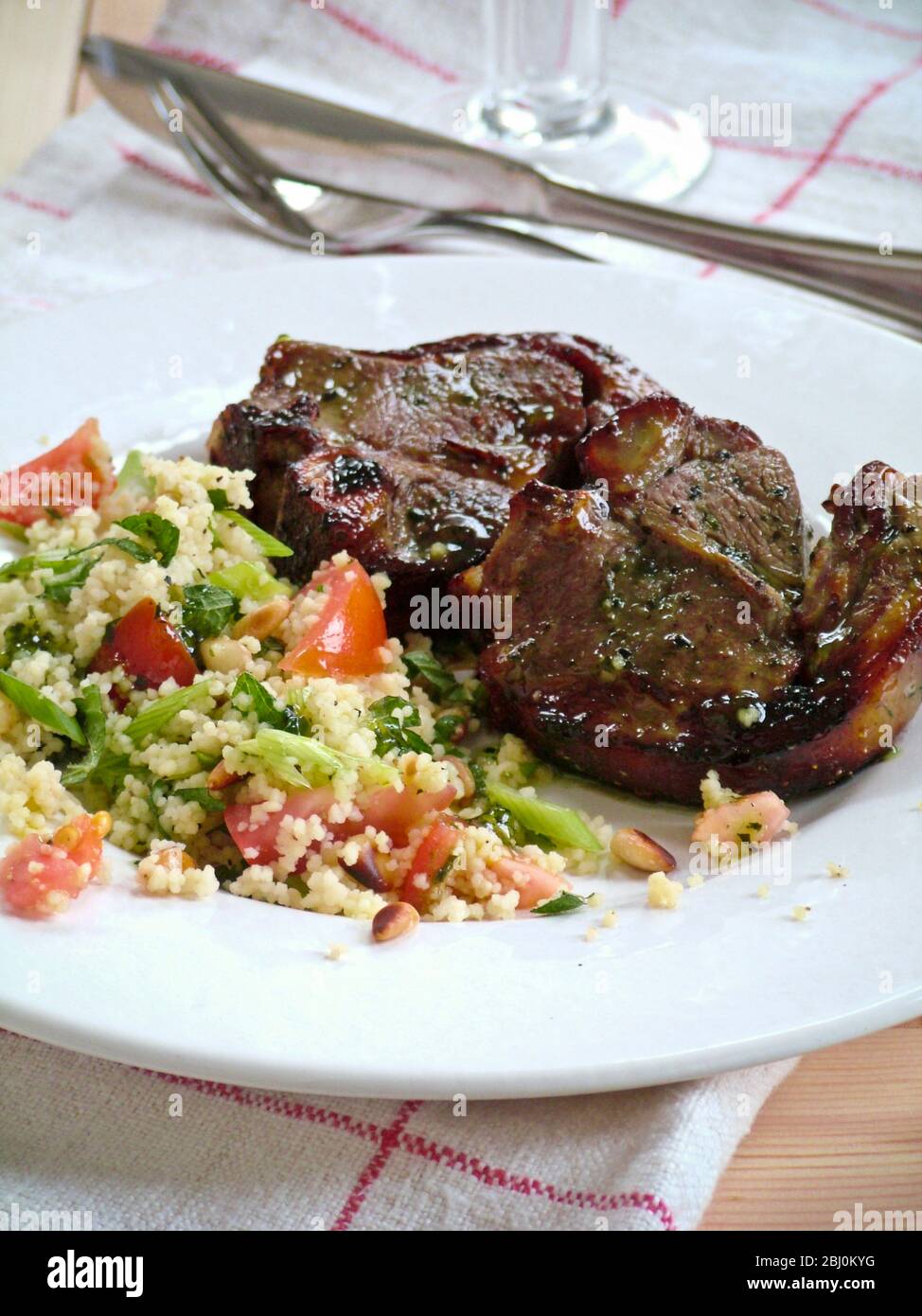 Due costolette di agnello con couscous con verdure su piatto bianco - Foto Stock