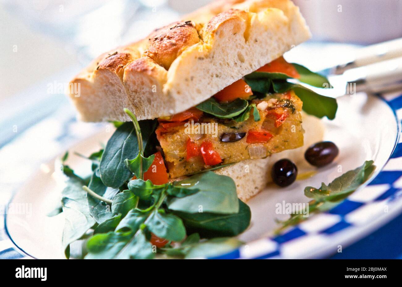 Sandwich di frittata spagnola in focaccia con insalata di rucola e olive nere - Foto Stock