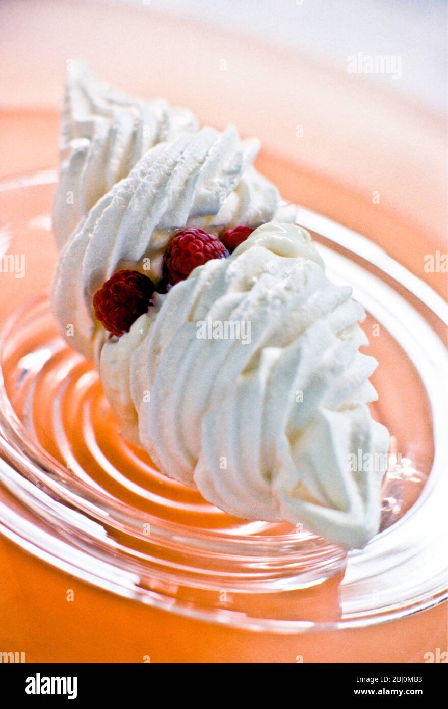 Meringhe racchiuse in sandwich con panna fresca e lamponi su un piatto di vetro. - Foto Stock
