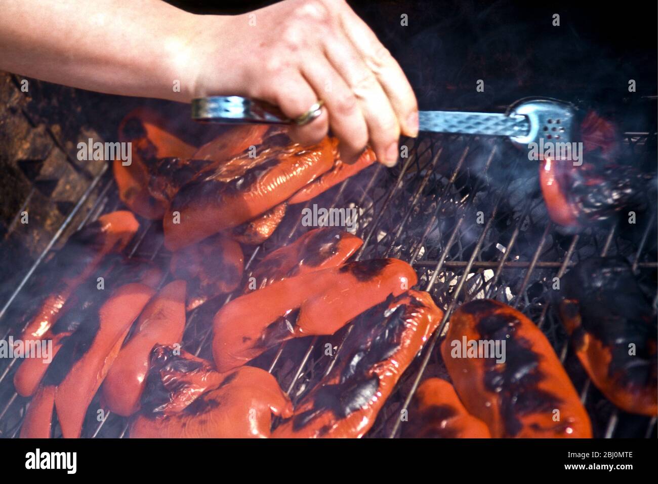Grigliare peperoni rossi su una griglia barbecue a carbone - Foto Stock
