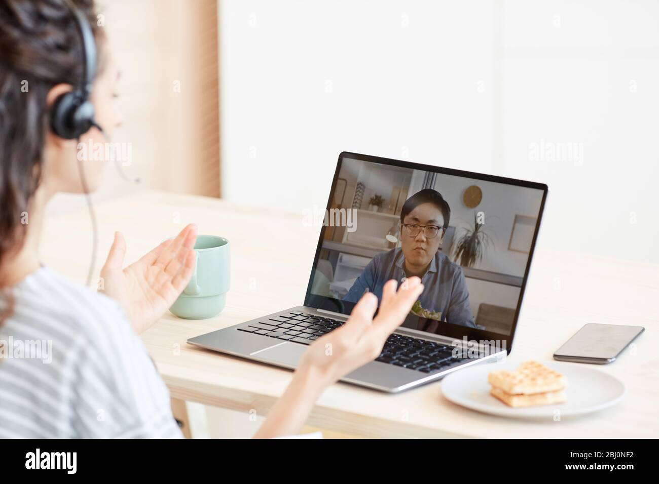 Giovane donna seduta al tavolo in cucina a discutere con il suo collega di qualcosa utilizzando la videochiamata Foto Stock