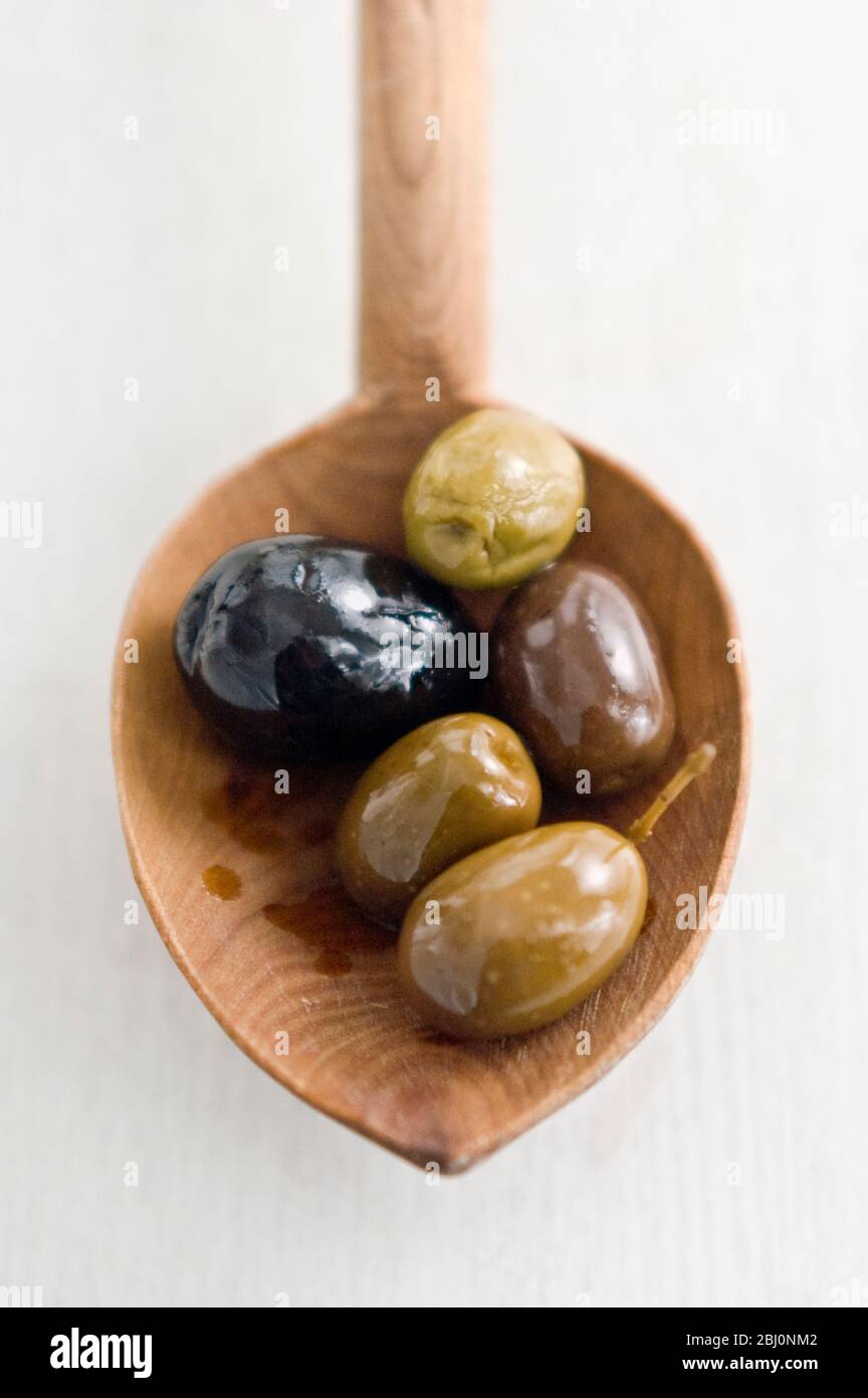 Selecion di varie buone olive intere su cucchiaio rustico di legno - Foto Stock