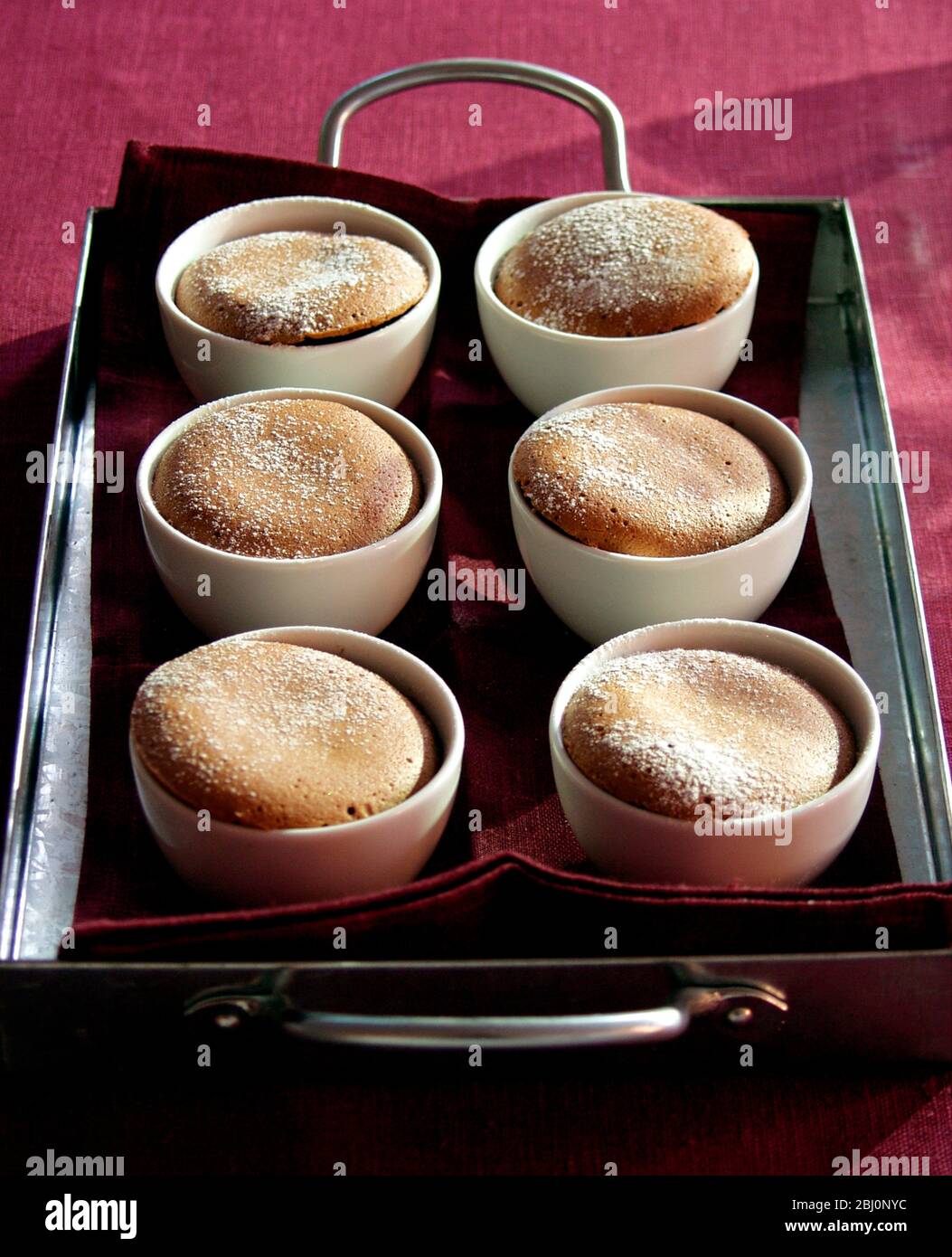 Sei budini di cioccolato al vapore serviti su vassoio metallico rivestito con tovagliolo di lino - Foto Stock