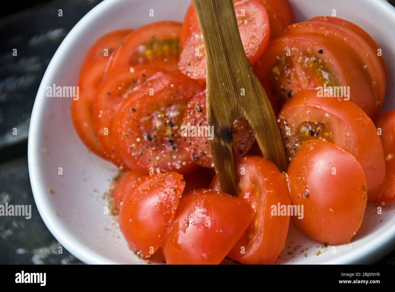 Insalata semplice di pomodori ciliegini con olio d'oliva e pepe a balsamo in un piatto di lizze con forchetta di legno - Foto Stock