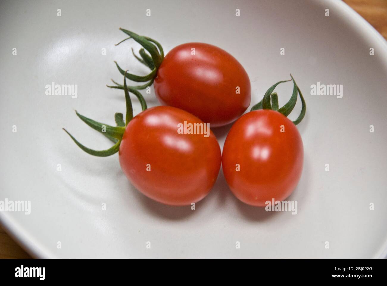 Tre tonatoes di susina coltivati in casa in piatto piccolo - Foto Stock