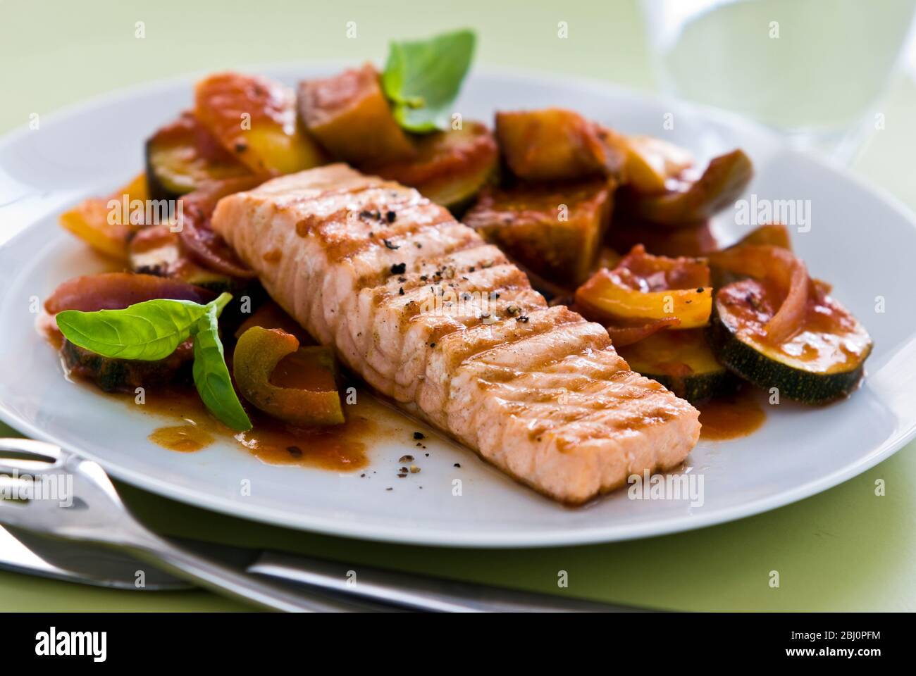Piccolo pezzo di filetto di salmone alla griglia, servito su ratatouille. Una singola portata su piatto bianco. Versione più nitida. - Foto Stock