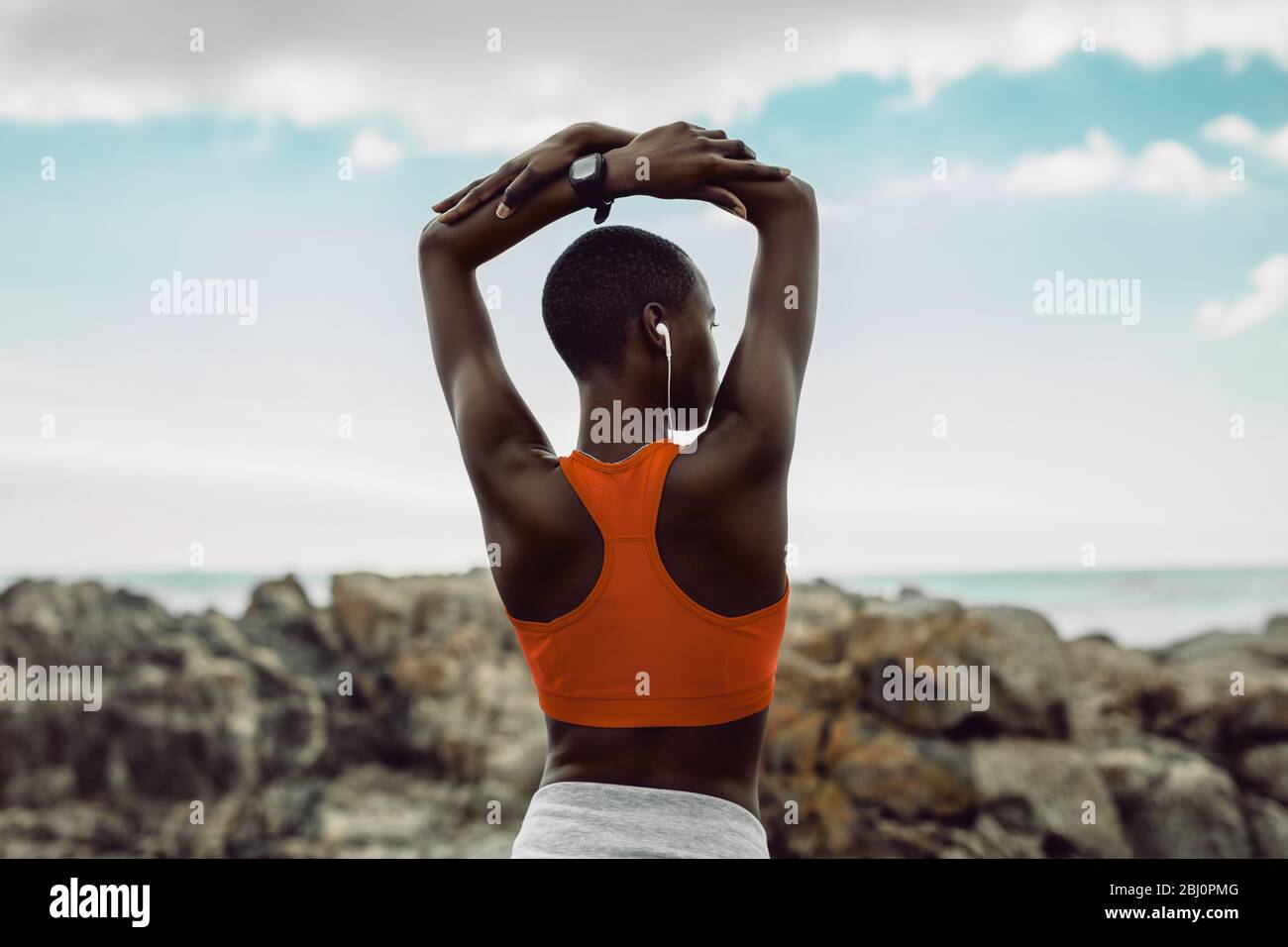 Vista posteriore della donna africana che fa l'addestramento di idoneità. Donna in fitness indossare esercizi di stretching con le braccia sollevate sopra la testa alla spiaggia. Foto Stock