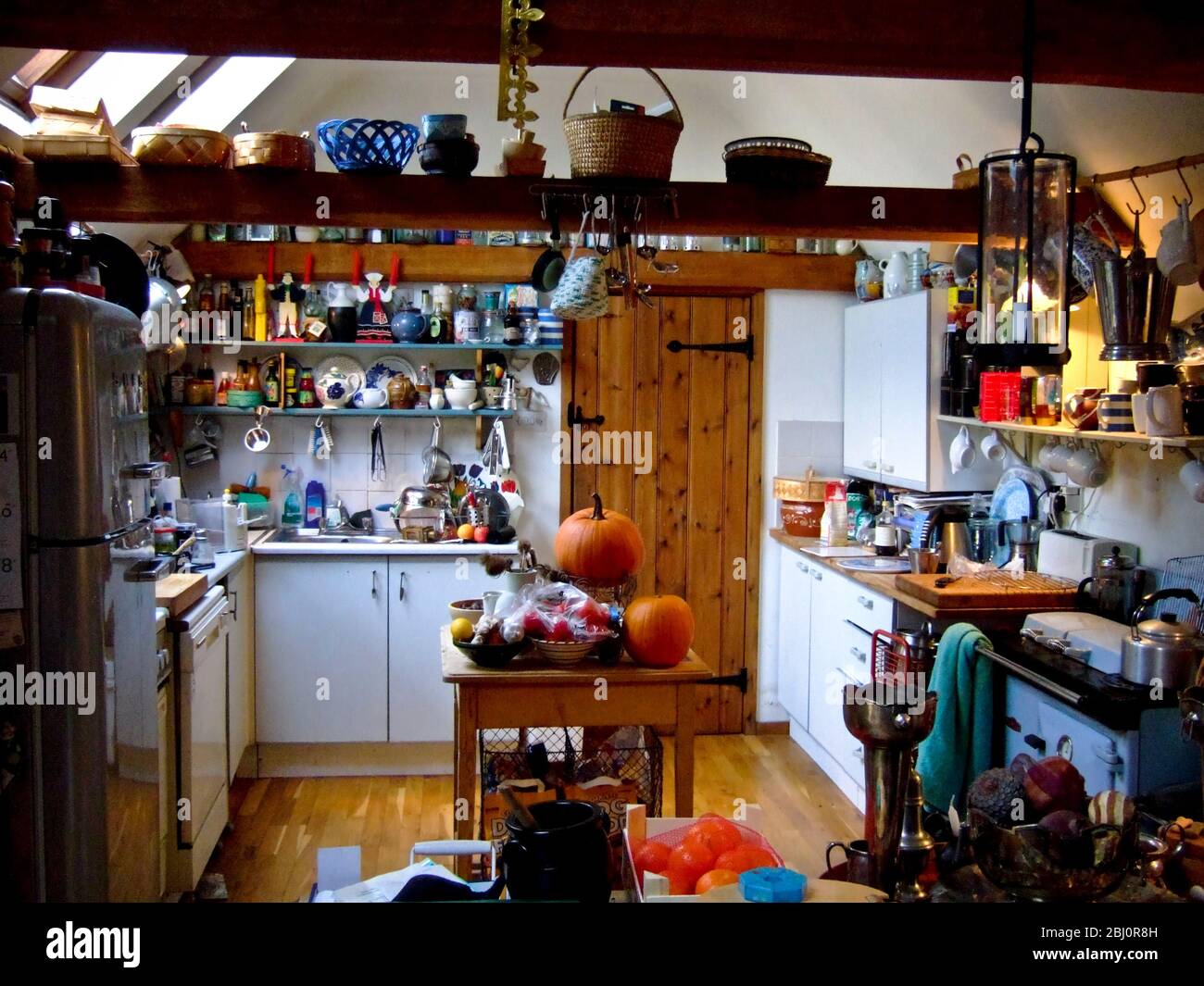 Cucina di campagna con stufa a petrolio Rayburn, moderno frigorifero retro Smeg, e un sacco di roba, cestini, verdure, ecc - Foto Stock