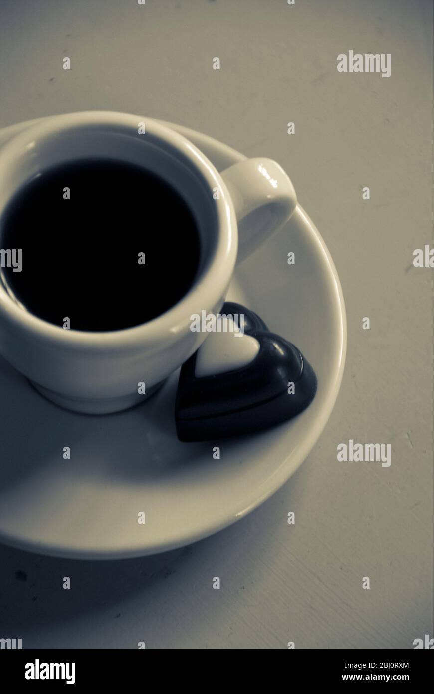 Cioccolato a forma di cuore su piattino di piccola tazza di caffè nero - Foto Stock