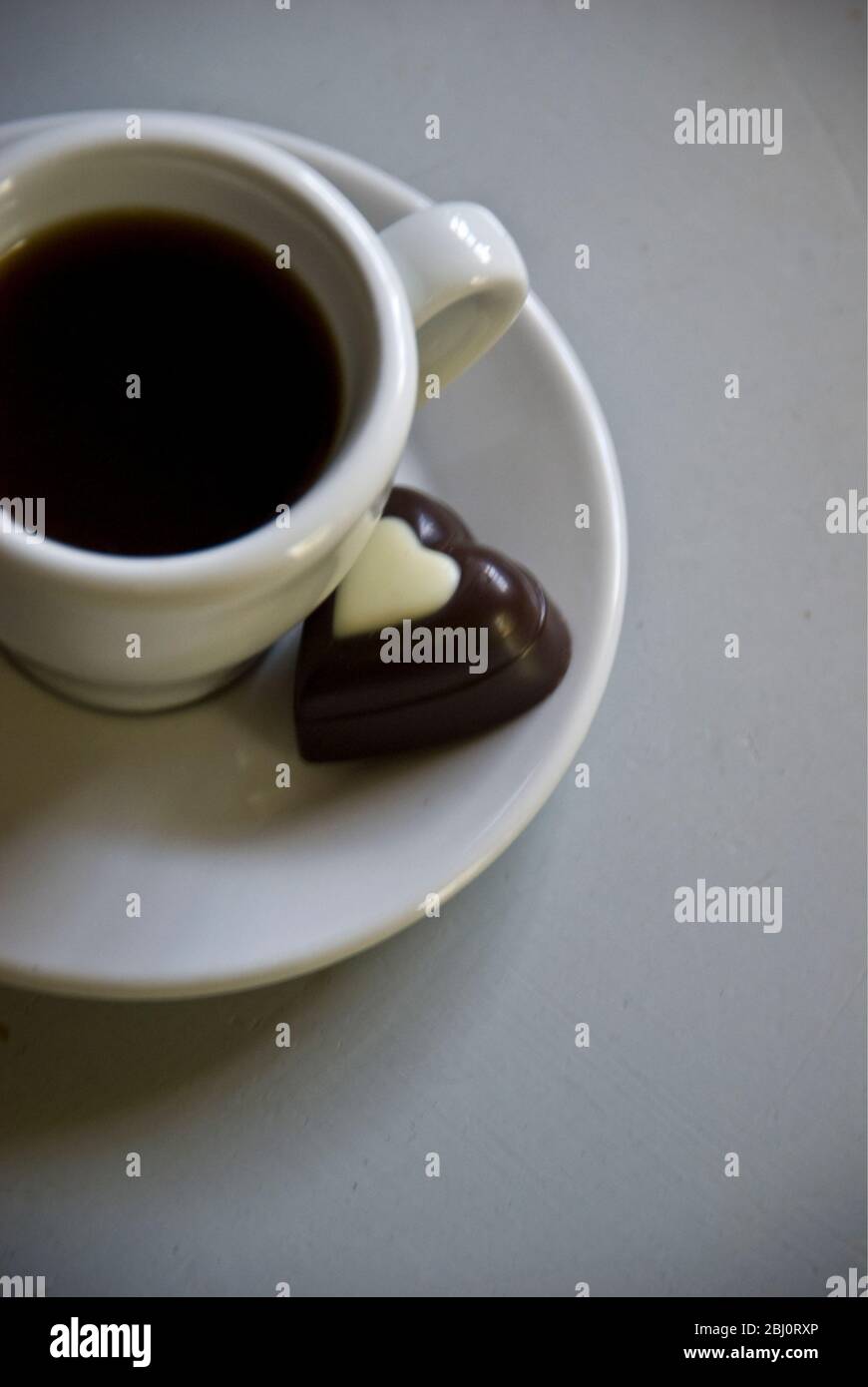 Cioccolato a forma di cuore su piattino di piccola tazza di caffè nero - Foto Stock