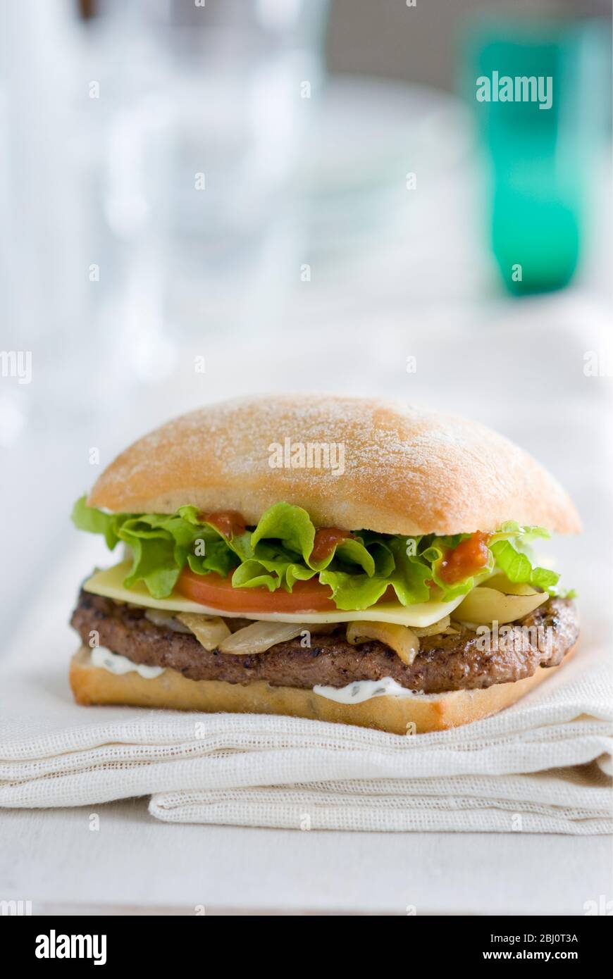 Cheeseburger con insalata e pomodoro su panino di ciabatta su tovagliolo bianco - Foto Stock