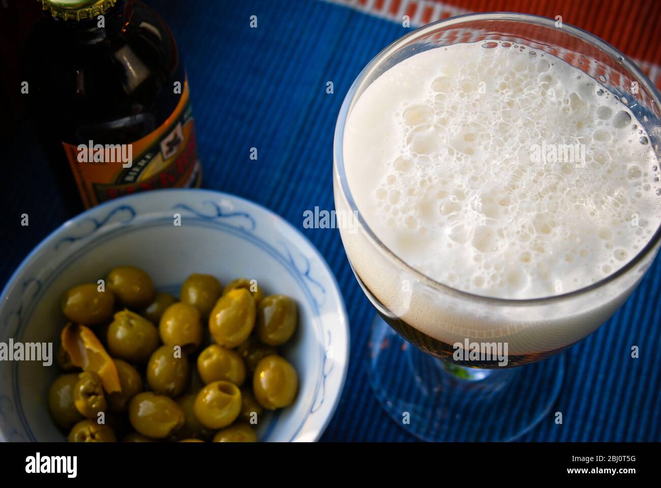 Bicchiere di birra con una buona testa di schiumatura e una ciotola di olive - Foto Stock