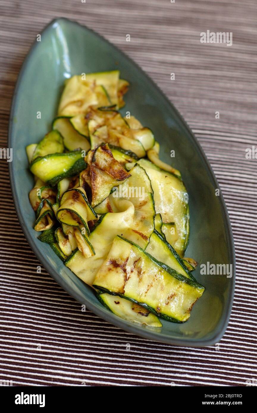 Zucchine a fette sottili cotte su una griglia, spazzolate con olio d'oliva e servite su un piatto verde - Foto Stock