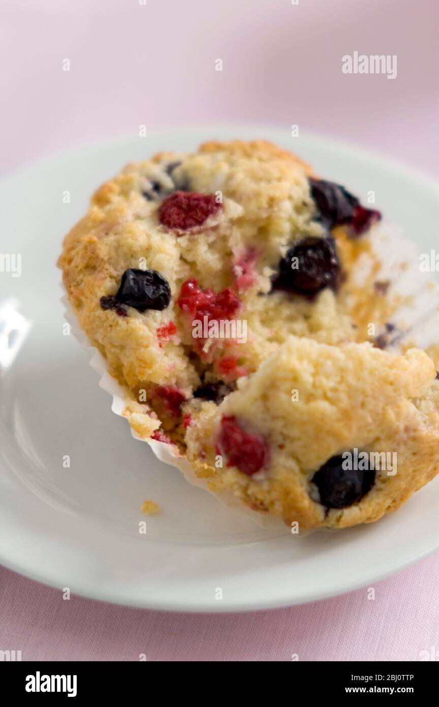 Muffin di bacche fresche con lamponi e mirtilli, strappato aperto su piatto bianco su panno rosa - Foto Stock