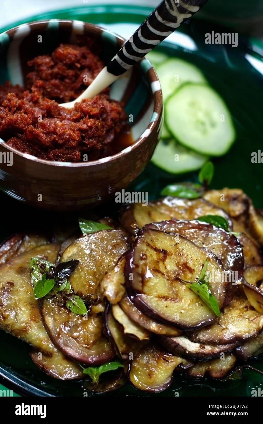 Ciotola di pomodori secchi tuffati con insalata di melanzane alla griglia con origano, su piatto di vetro verde - Foto Stock