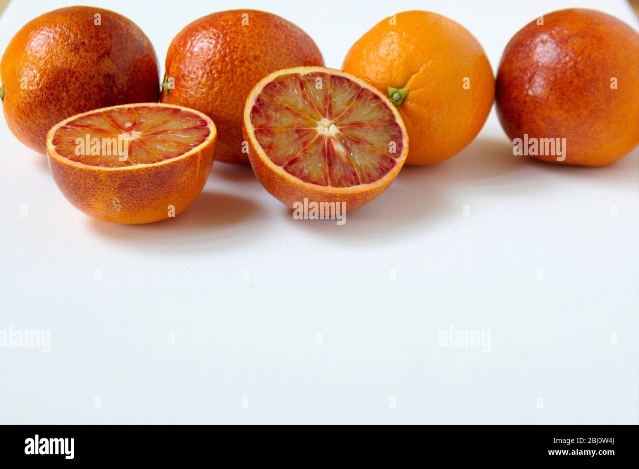 Arancione sangue, tagliato a metà su superficie bianca con arance intere dietro - Foto Stock