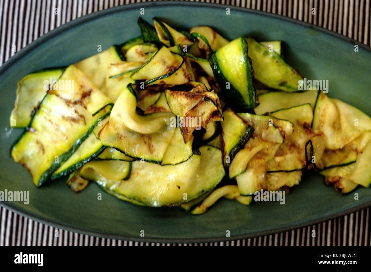 Zucchine a fette sottili cotte su una griglia, spazzolate con olio d'oliva e servite su un piatto verde - Foto Stock