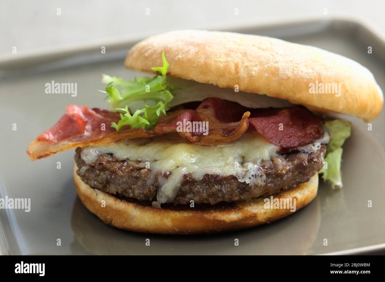 Hamburger alla griglia in panino con insalata di frisee, pancetta alla griglia e formaggio fuso - Foto Stock