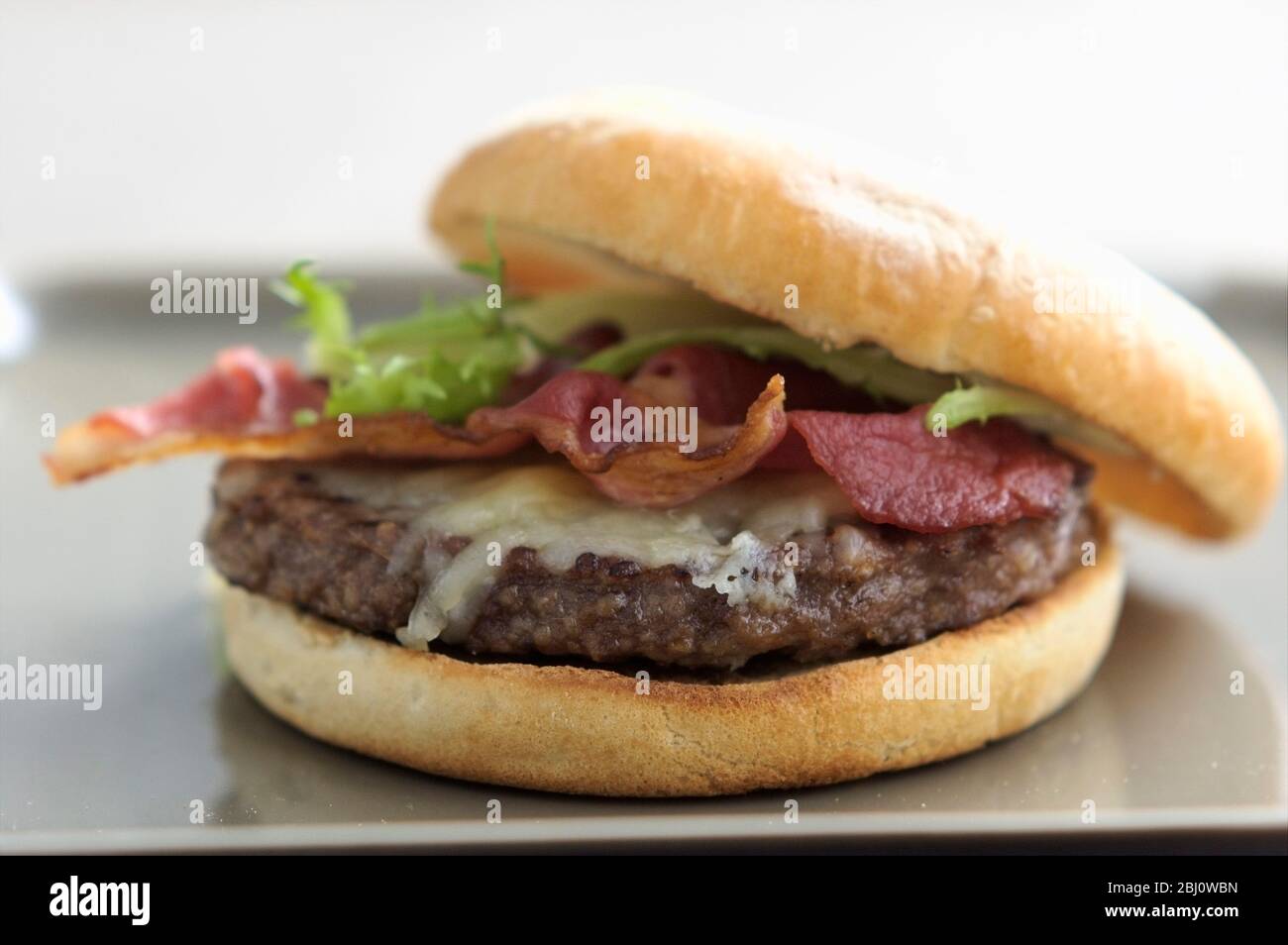 Hamburger alla griglia in panino con insalata di frisee, pancetta alla griglia e formaggio fuso - Foto Stock