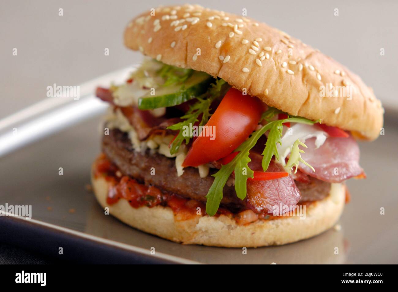 Hamburger alla griglia in panna con insalata di frisee, salsa di pomodoro, zeppa di pomodoro e rasatore di pancetta alla griglia e panna acida - Foto Stock