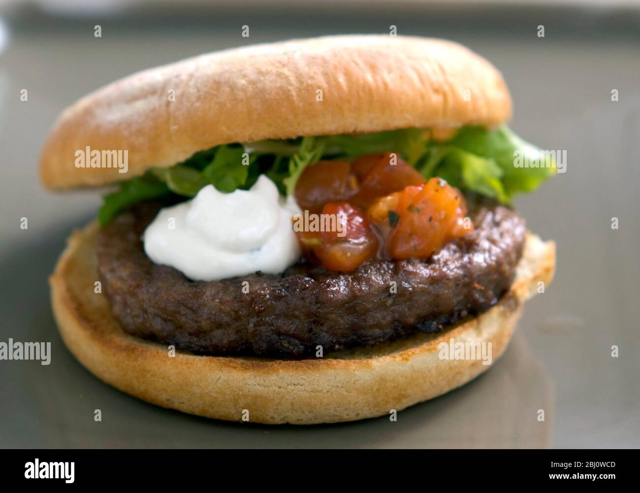 Hamburger alla griglia in panna con insalata di frisee, salsa di pomodoro e panna acida - Foto Stock