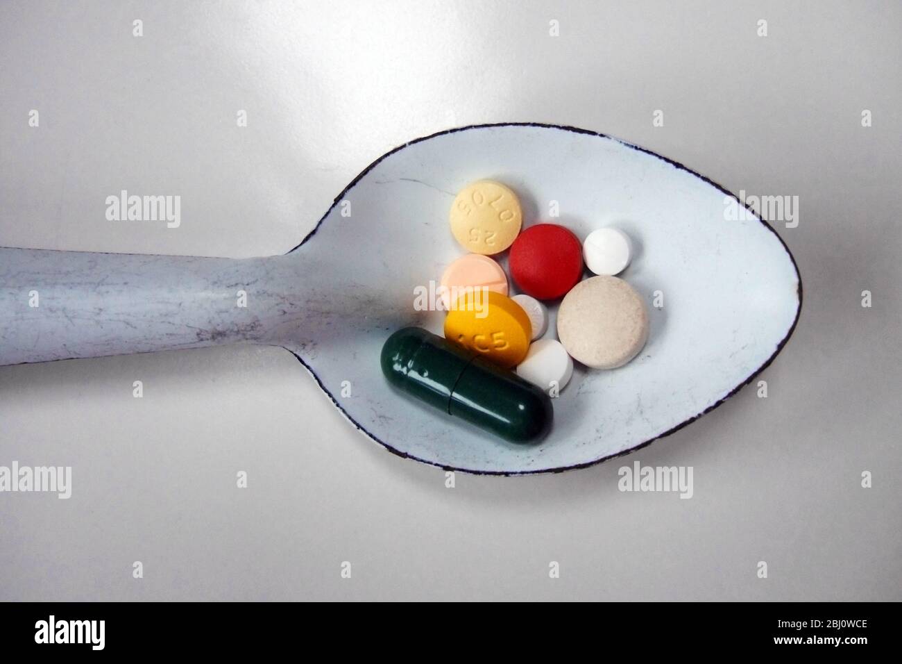 Cucchiaio di smalto bianco di varie pillole colorate - Foto Stock