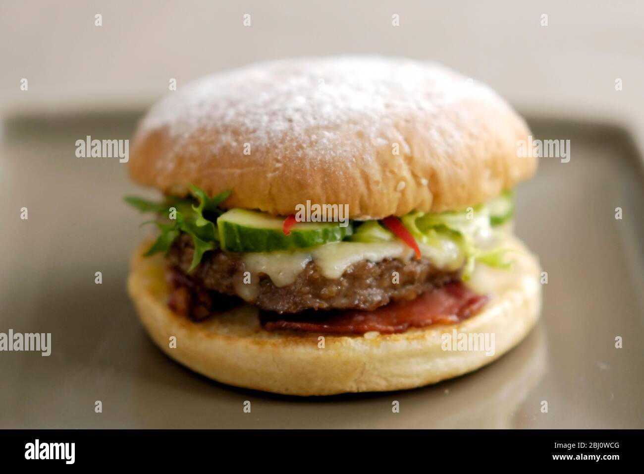 Hamburger alla griglia in panino con insalata di frisee, cetrioli, strisce di pepe, formaggio fuso, pancetta alla griglia e salsa di pomodoro - Foto Stock