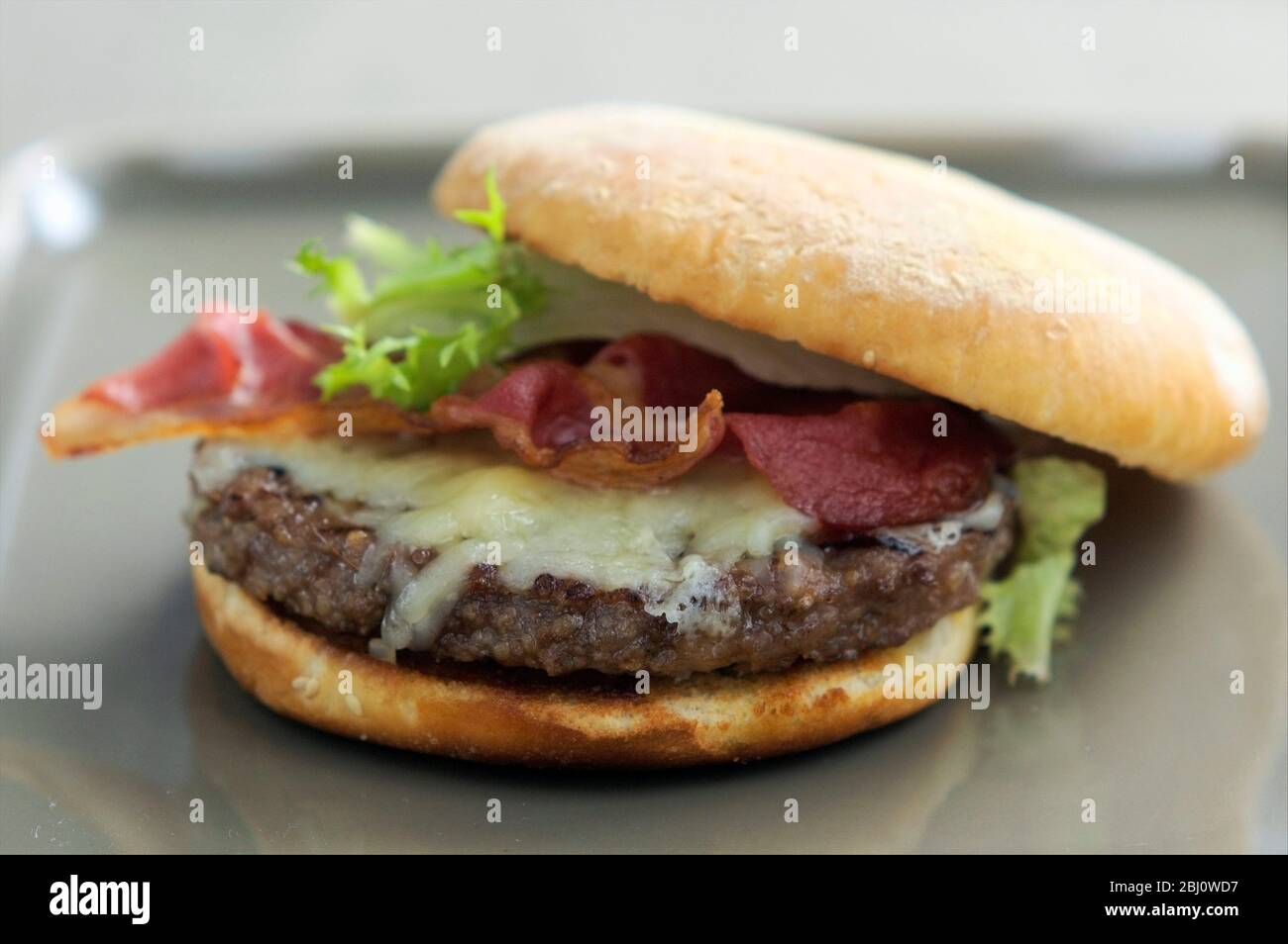 Hamburger alla griglia in panino con insalata di frisee, pancetta alla griglia e formaggio fuso - Foto Stock