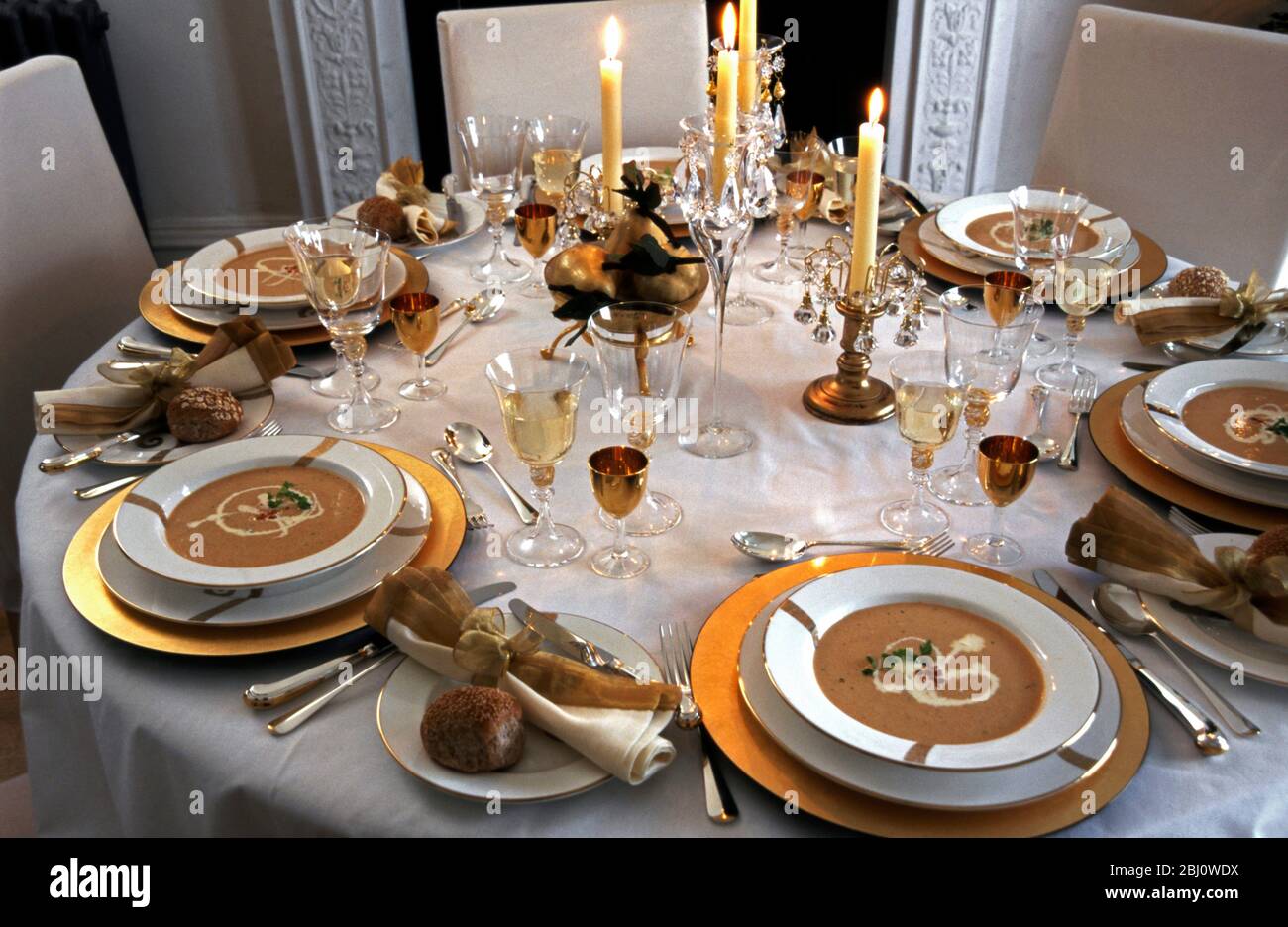 Formale cornice per festa tavolo per festa o festa di nozze con zuppa in grandi bocce aperte su piatto orlato su piatti dorati con candele e. Foto Stock